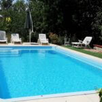 piscine et chaises transats blanches au bord avec un parasol fermé